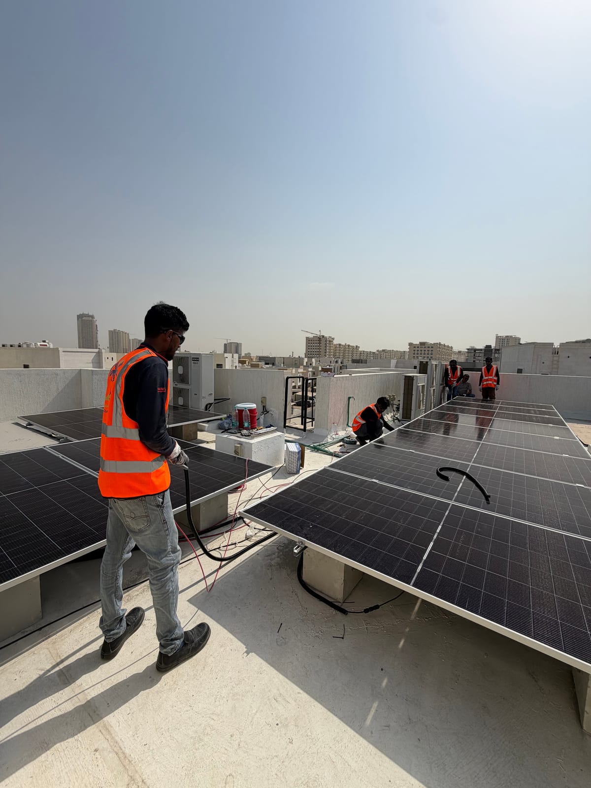A Solar Oasis crew member running a cable along the solar array on a villa roof, three more of the crew at work beyond, Ajman