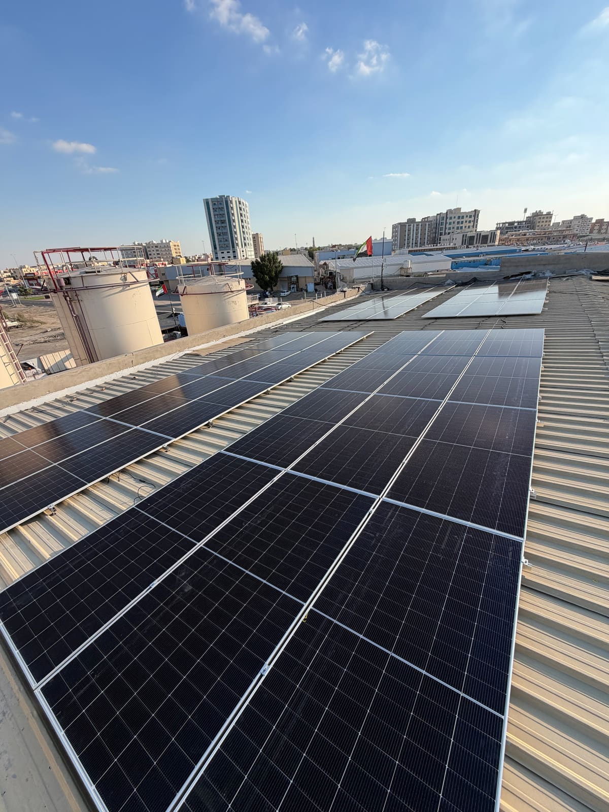 Rows of solar panels on the metal roof of a commercial building under a blue sky, Al Jurf, Ajman