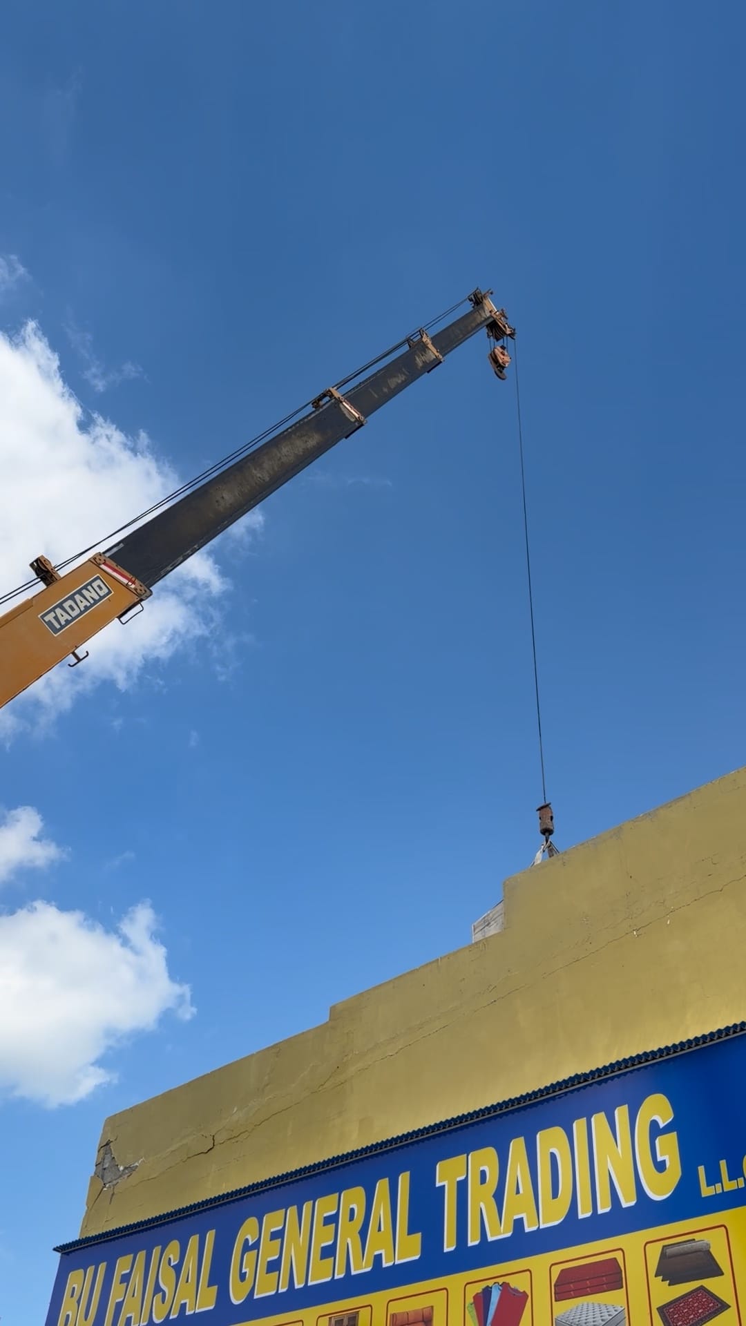 Crane boom with its hook at the roof edge during delivery to the roof, above the Bu Faisal General Trading shopfront, Al Jurf, Ajman