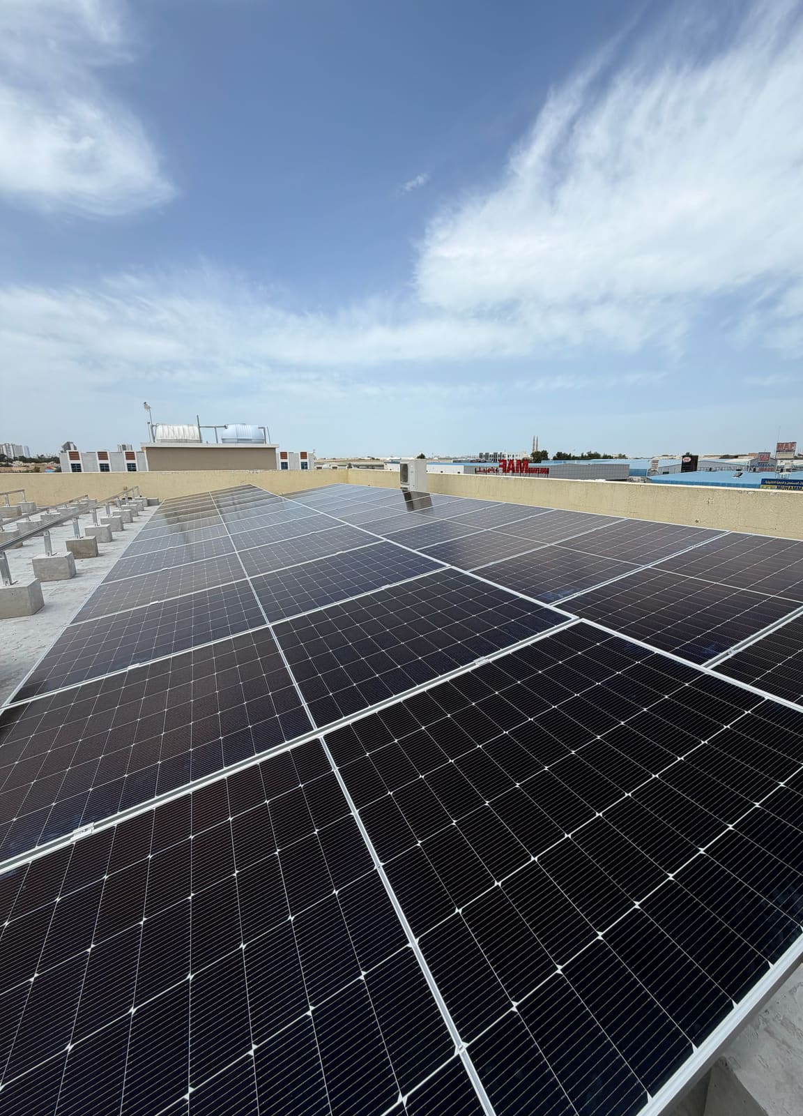 Solar array on ballast blocks on a flat concrete roof under high cloud, Al Jurf, Ajman