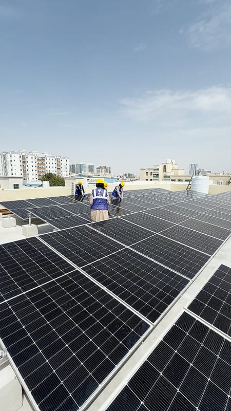 Solar Oasis crew in hard hats, branded vests and gloves installing panels on a flat concrete roof, Al Jurf, Ajman