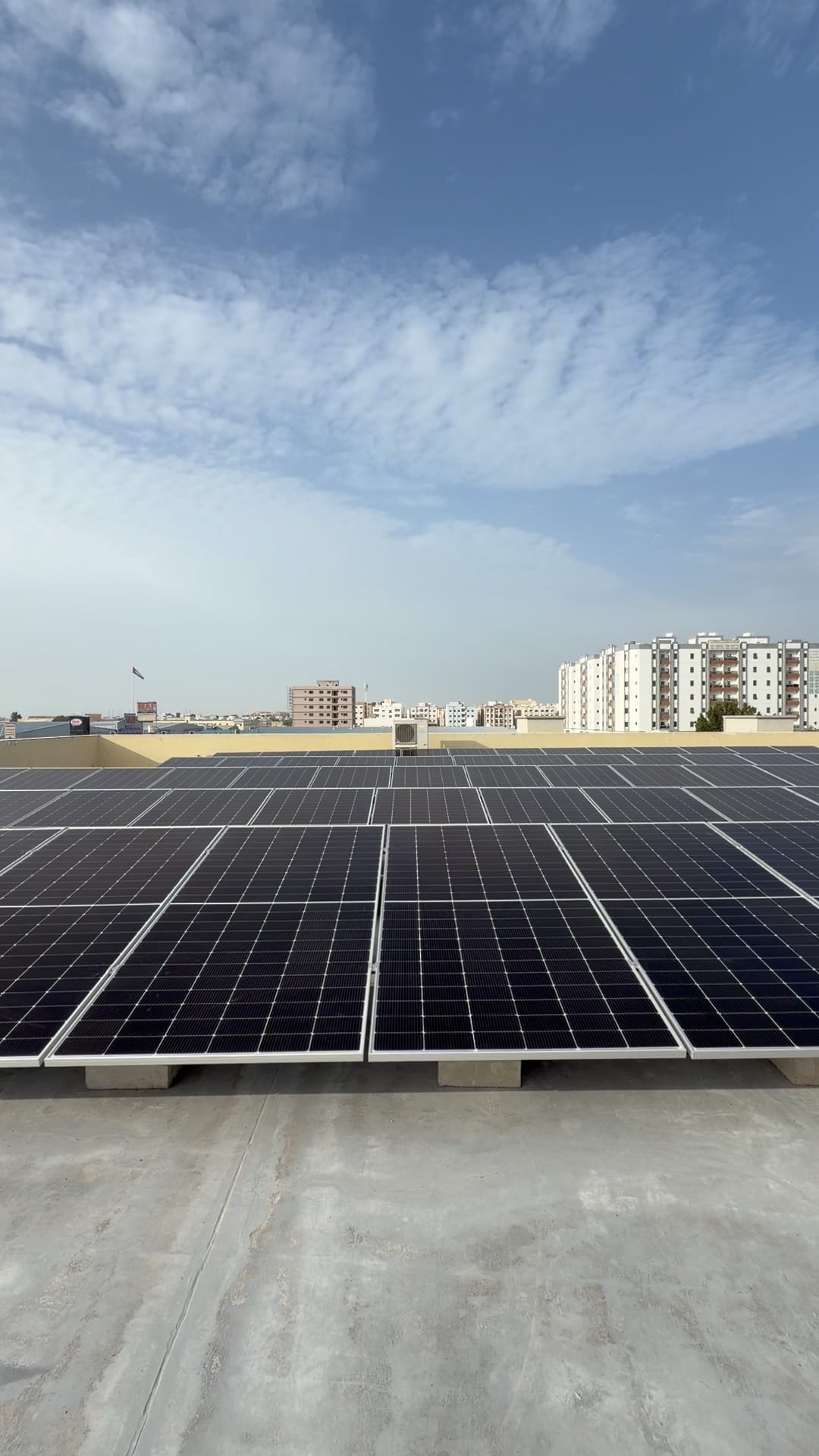 Finished solar array on ballast blocks on a flat roof under high cloud, Al Jurf, Ajman