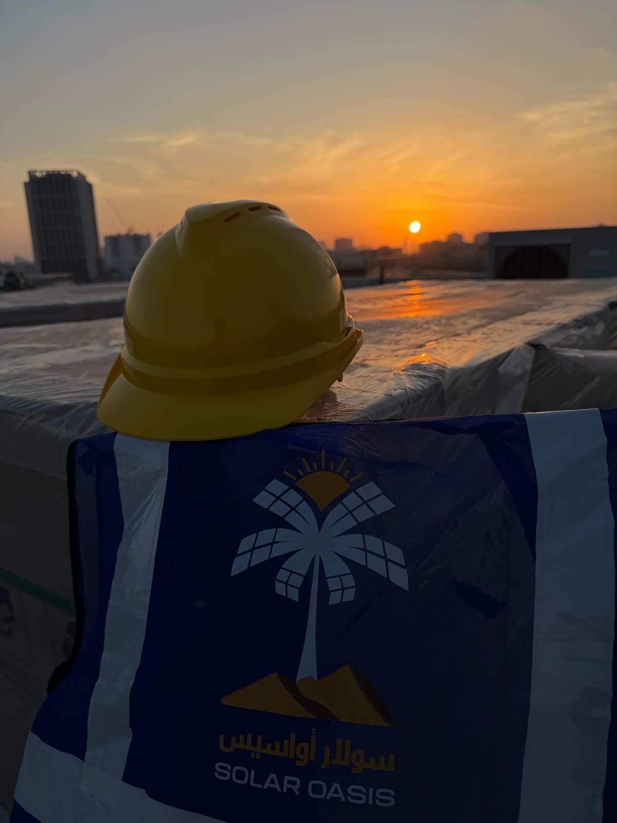 A hard hat and a Solar Oasis hi-vis vest resting on wrapped pallets on a roof at sunset