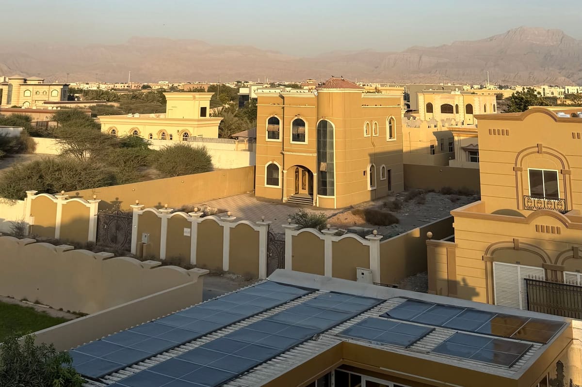 Solar panels on a low roof of a villa in Ras Al Khaimah, with neighbouring villas and the Hajar Mountains behind