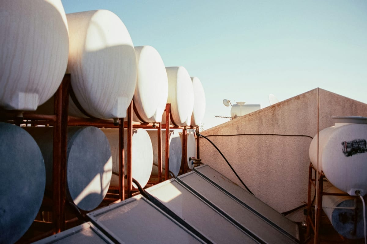 Solar water heaters on a flat roof: flat-plate collectors in front of a row of white storage tanks